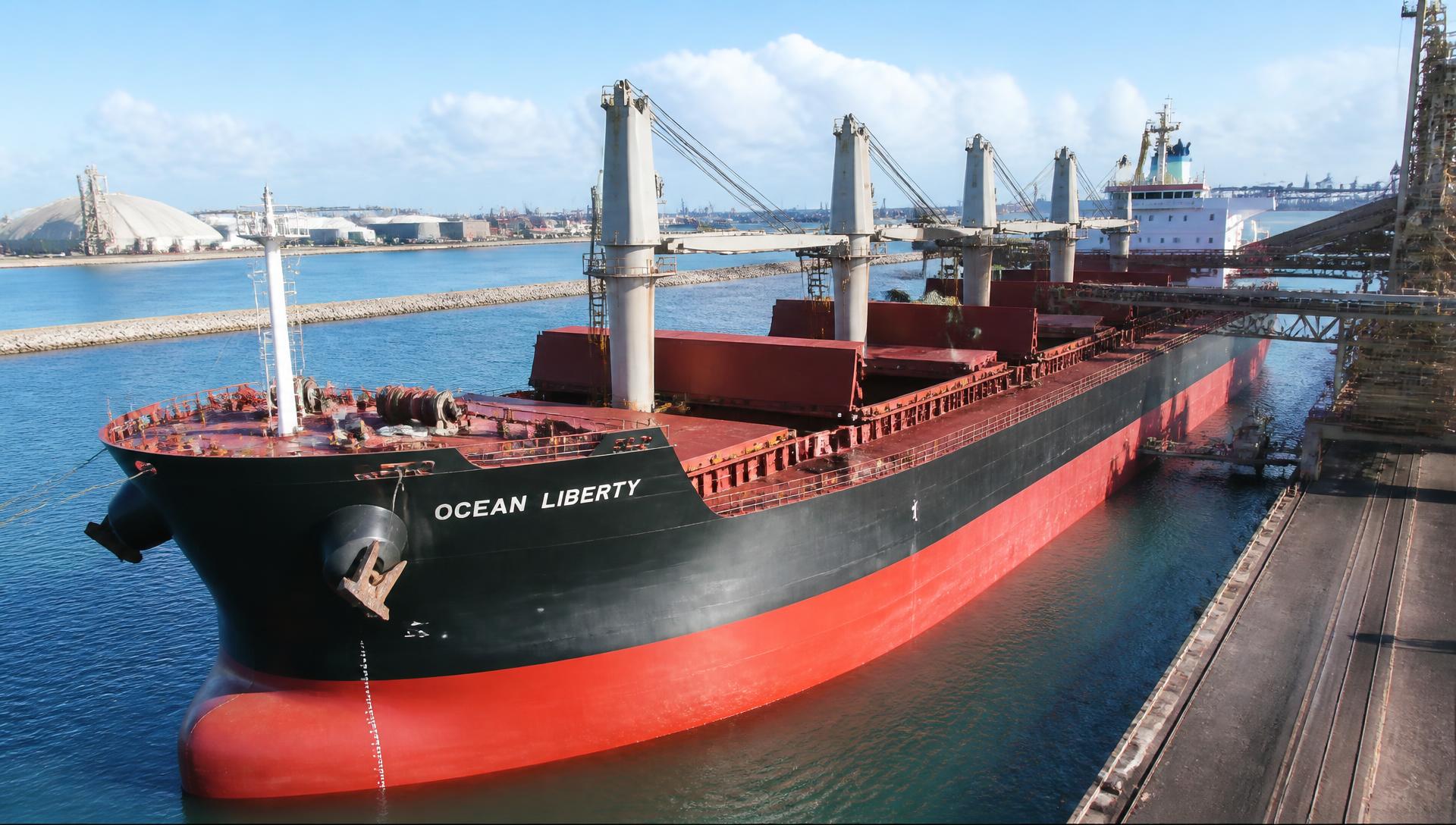 Ultramax geared dry bulk carrier with deck cranes alongside a bulk terminal